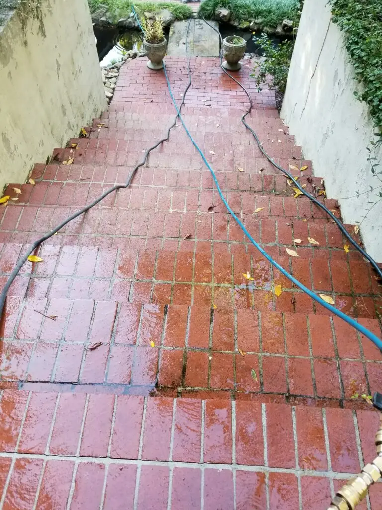 Red brick walkway being pressure washed, showing the cleaned strip next to the dirty brick