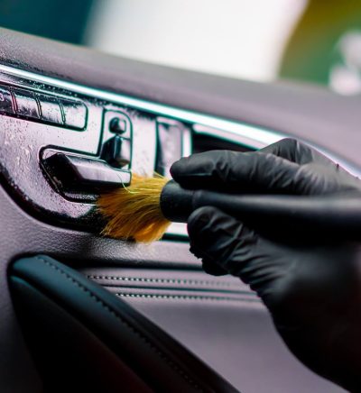 Detailer using a soft brush to clean the dashboard vents and controls of a car interior